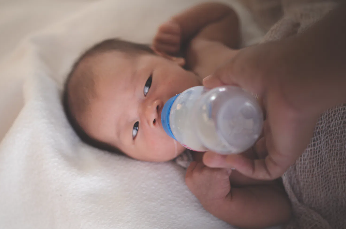 Newborn lying in bed and being fed milk by bottle.