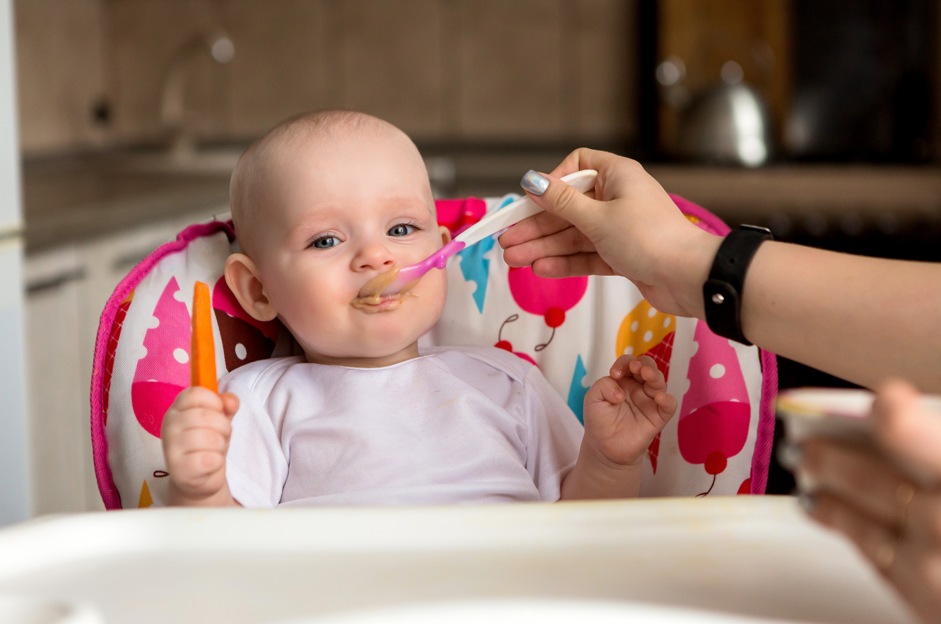 Baby being fed in high-chair with a spoon.