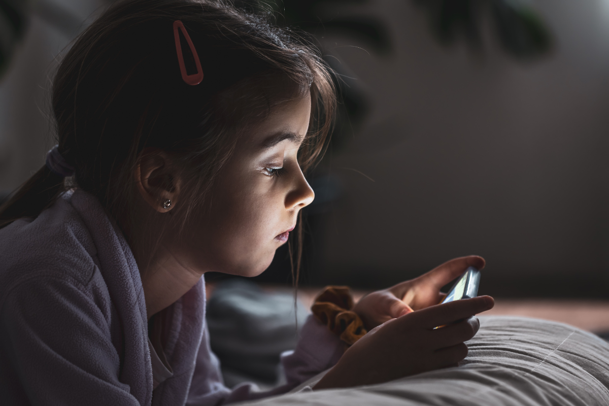 A young, sad looking girl scrolling through socail media on her phone alone in her bedroom in Austin, Texas.